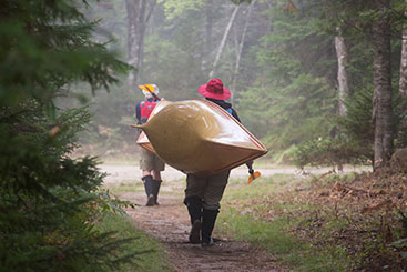 Two people carrying their kayaks through a trail. Gifts of Real Estate